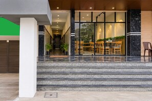 Ein moderner Gebäudeeingang mit einer Treppe zu einem Essbereich, der Holzmöbel und Topfpflanzen beinhaltet.