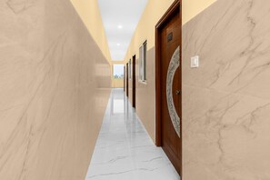 Un pasillo con paredes de mármol y suelo reflectante, que conduce a una puerta con una placa de número.