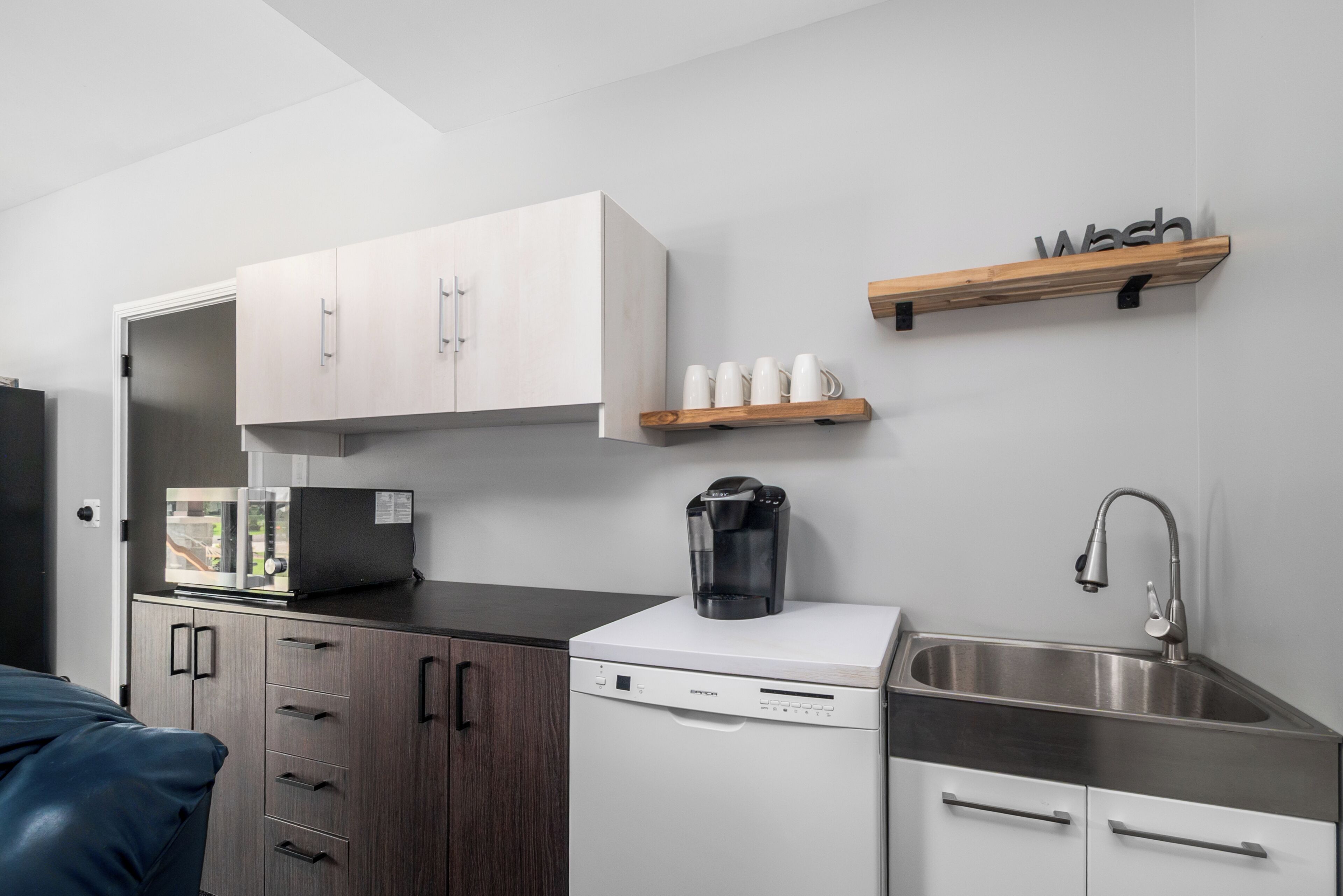 Una cocina compacta con armarios blancos, una cafetera y un lavamanos.