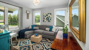 A living room with a sectional sofa, a small ottoman, a potted plant, a mirror, and a chandelier.