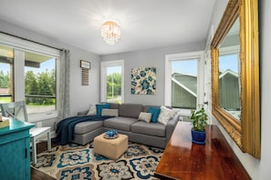 A living room with a sectional sofa, a small ottoman, a potted plant, a mirror, and a chandelier.