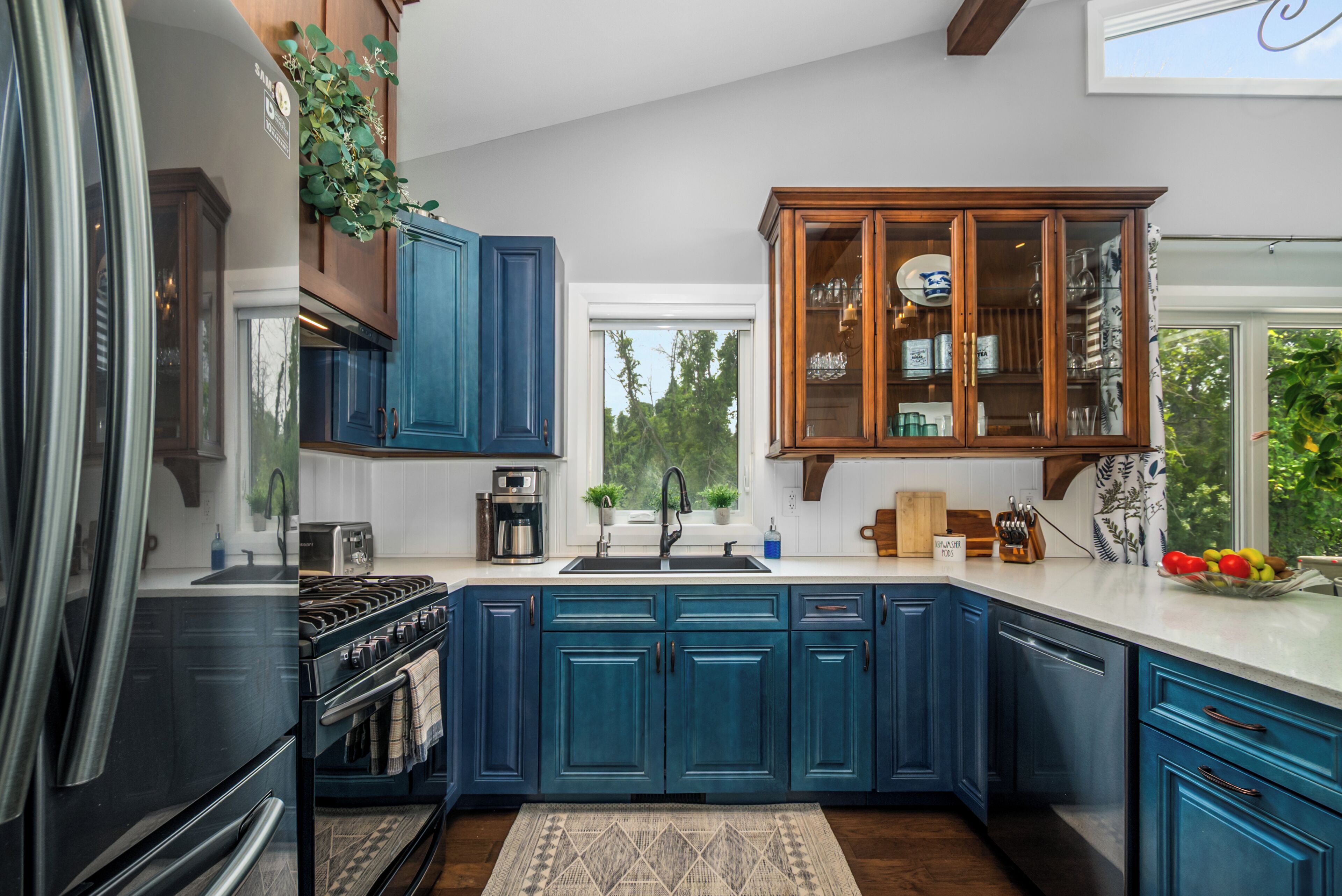 A kitchen with blue cabinets, a built-in oven, a coffee maker, and a fruit bowl on the counter.