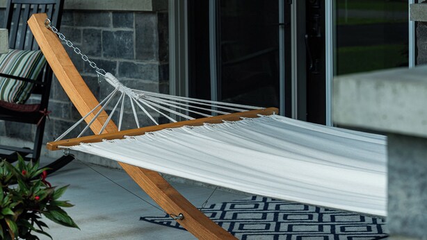 A hammock suspended between a wooden frame, set on a concrete floor with a patterned rug.
