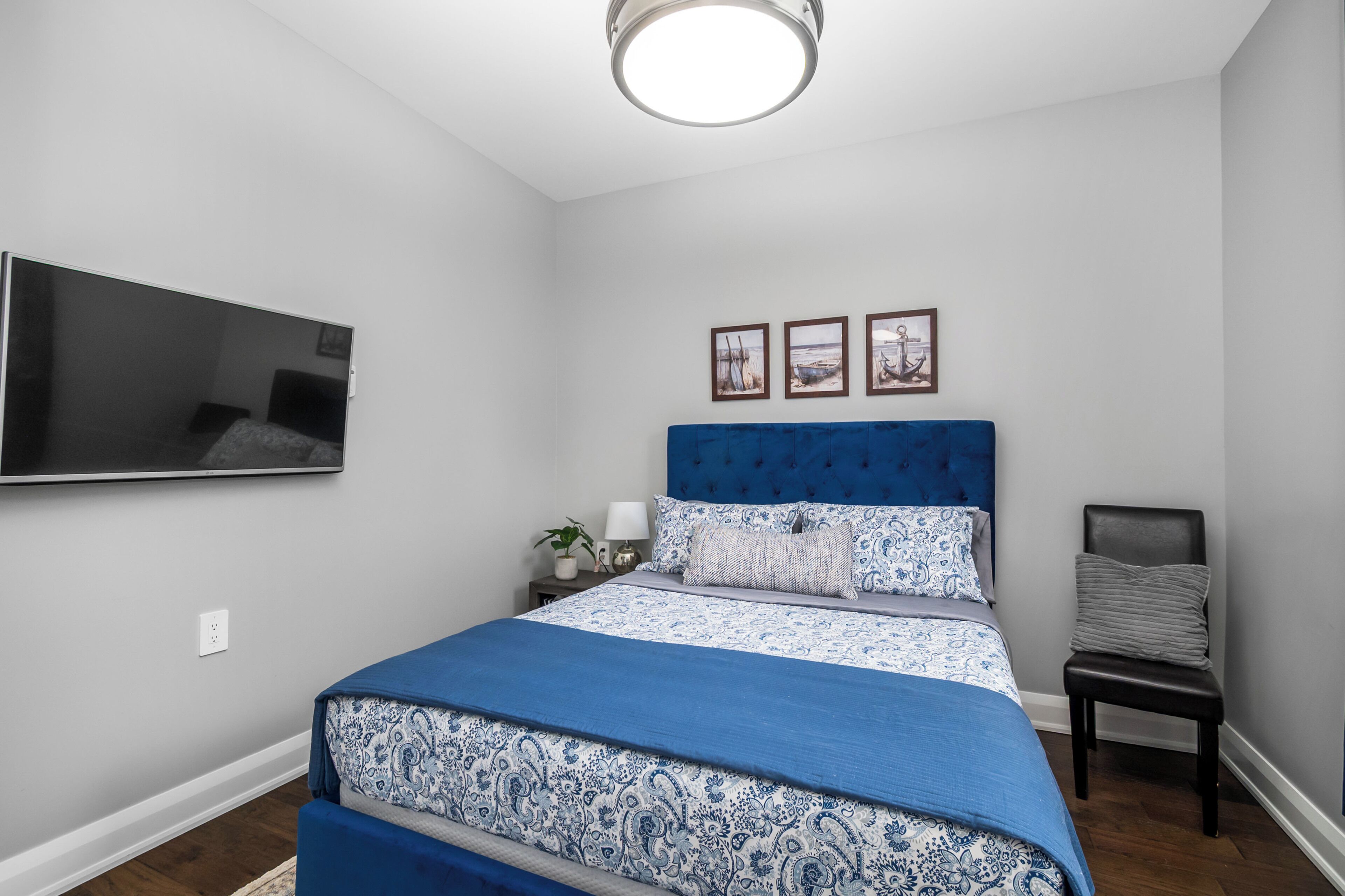 Une chambre à coucher comprenant un lit, un téléviseur à écran plat fixé au mur, une table de chevet avec une lampe et une chaise.