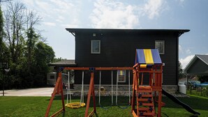 A playground with swings and a slide in front of a house.