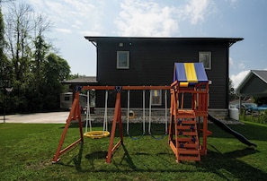 A playground with swings and a slide in front of a house.