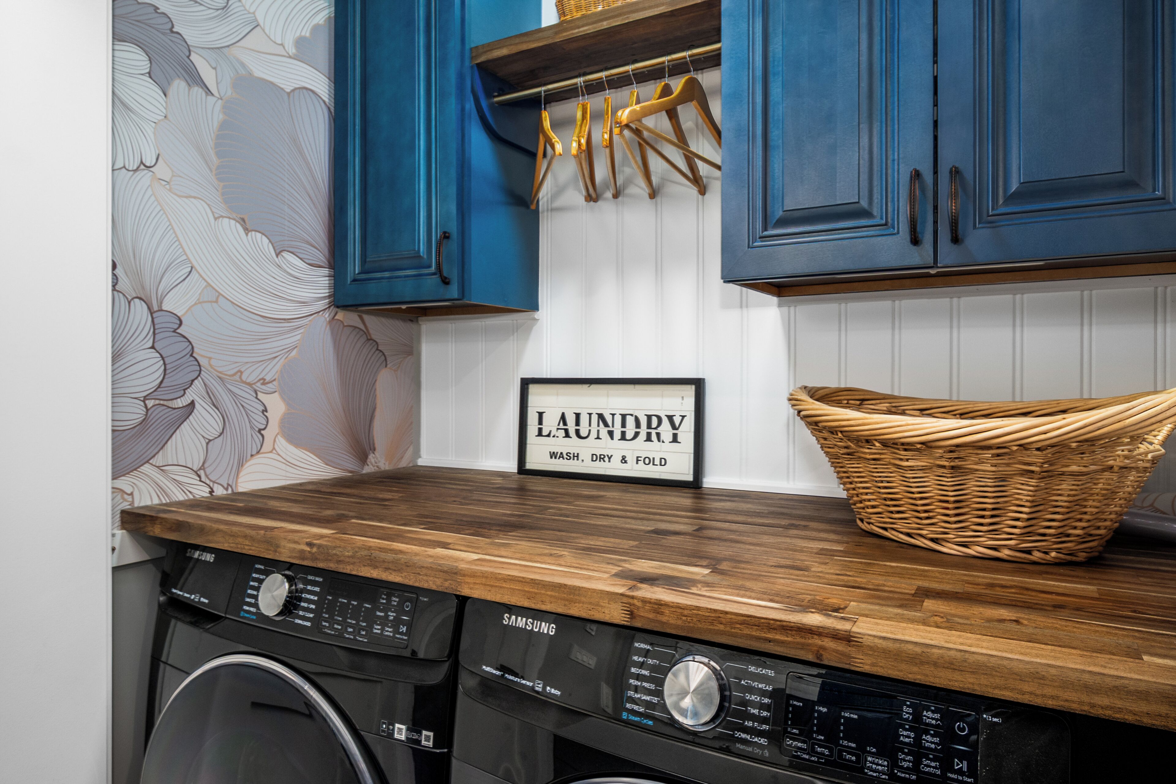 Un área de lavandería con una lavadora Samsung, una encimera de madera, una cesta de mimbre y un letrero que dice 'LAUNDRY WASH, DRY & FOLD'.