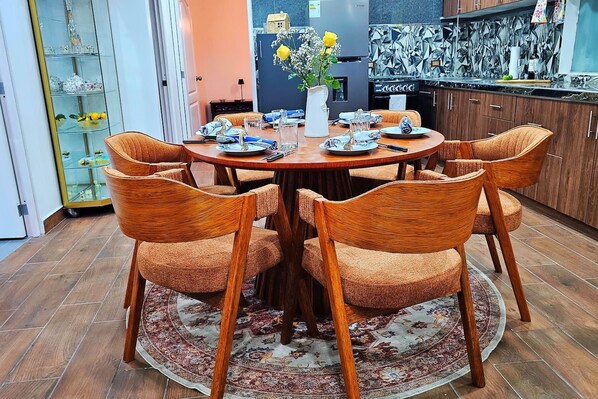 Un comedor con una mesa redonda, seis sillas de mimbre y un centro de mesa floral.