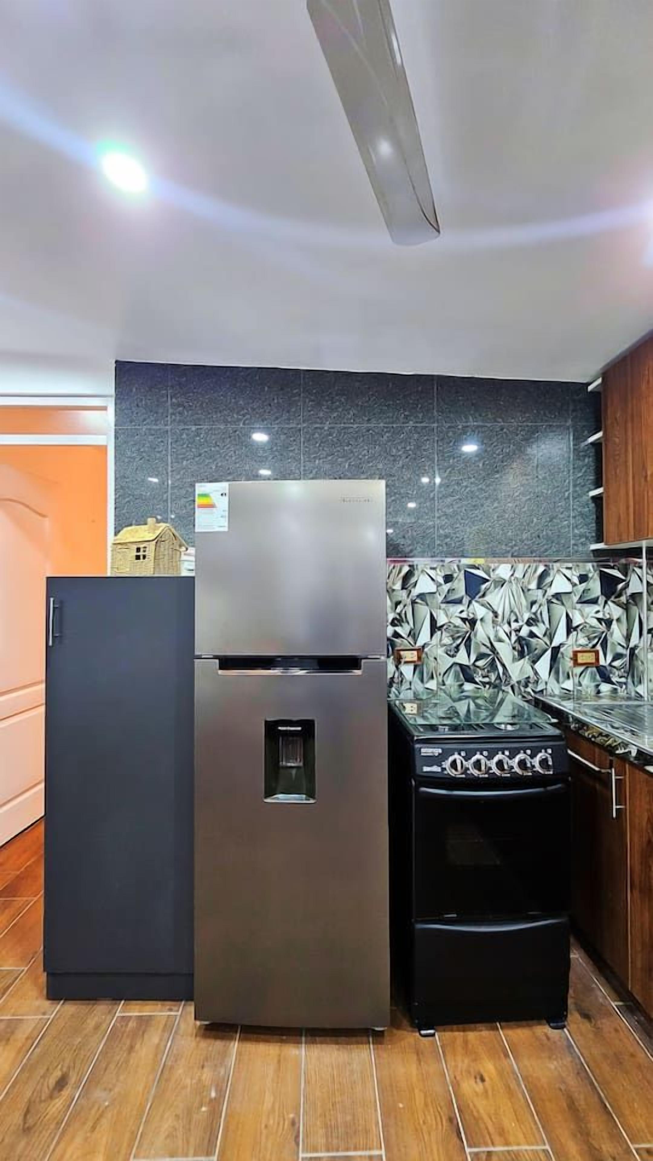 Cozinha com geladeira de aço inoxidável, forno preto e painel de azulejos.