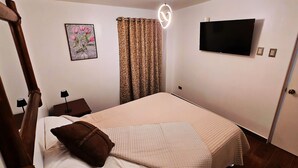 A bedroom with a bed, a television, a painting, and a curtain.