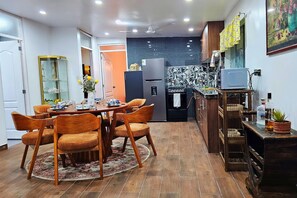 A dining area with a round table and chairs, a kitchen with a refrigerator and stove, and a small bar area with a television.