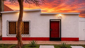 A building with a red door, a window with a metal grille, and a sign above the door.
