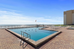 A rectangular pool with a metal ladder and a flagpole, surrounded by a white fence and a paved deck. - 🌊Top Floor 1BR Condo | Ocean + Pool Views | Sleeps 4 | Castle Reef 407🌊 (New Smyrna Beach)