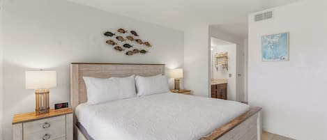 Une chambre à coucher avec une tête de lit en bois, un lit avec une literie blanche, deux tables de chevet avec des lampes, une horloge murale et un tableau décoratif représentant des poissons.