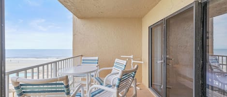 Un balcon avec vue sur la plage, équipé d’une table et de chaises.