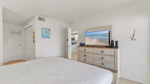 Une chambre à coucher avec un lit, une commode, un tableau et une porte sur laquelle est accroché un porte-manteau.