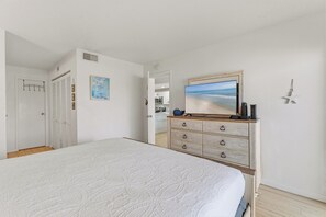 A bedroom with a bed, a dresser, a painting, and a door with a coat rack. - 🌊Top Floor 1BR Condo | Ocean + Pool Views | Sleeps 4 | Castle Reef 407🌊 (New Smyrna Beach)