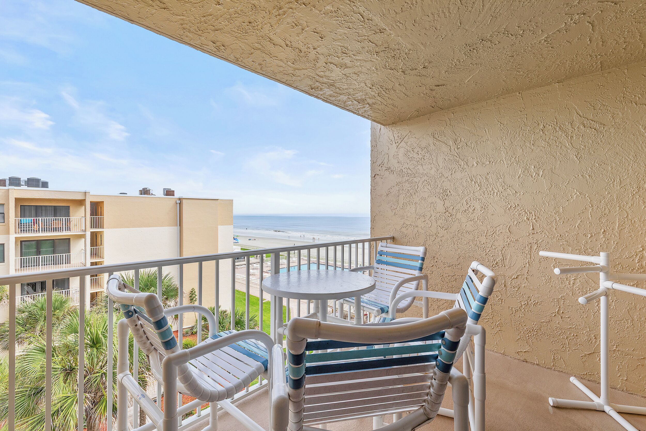 Een balkon met uitzicht op het strand, een ronde tafel en twee streepstoelen.