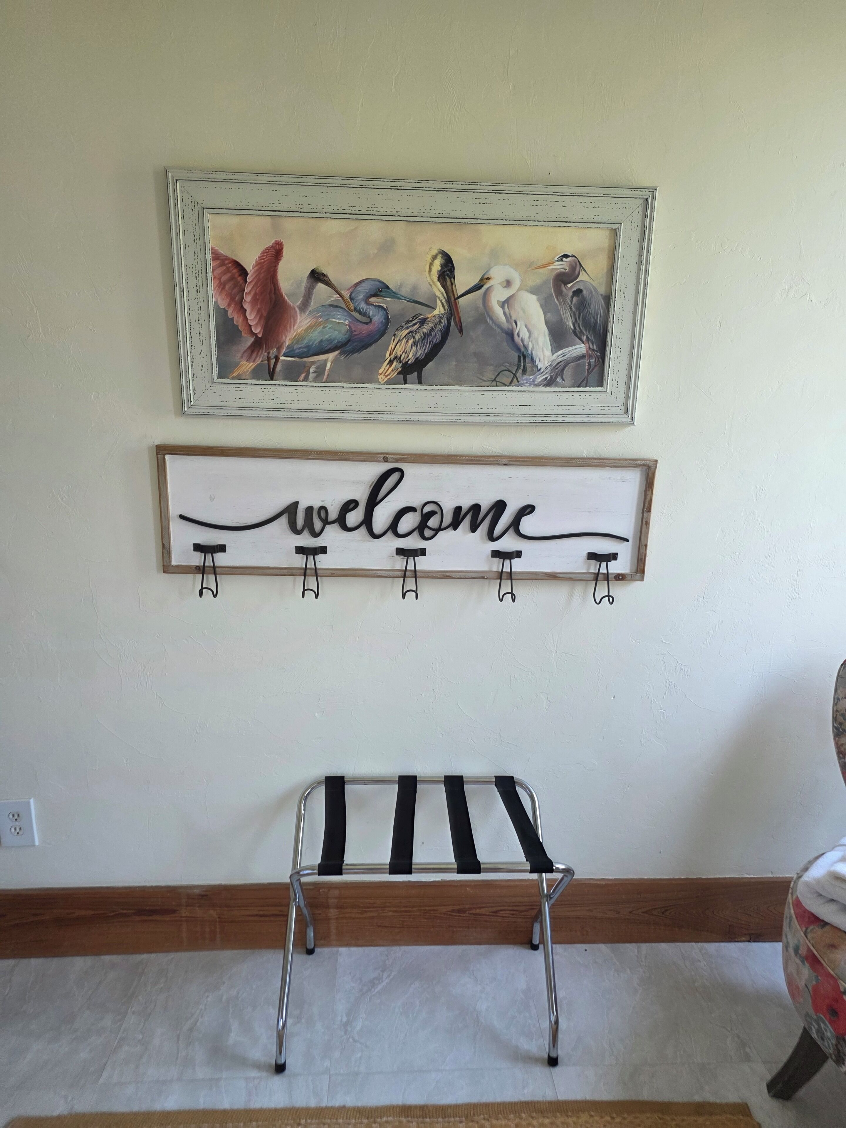 A wall with a framed painting of birds, a 'welcome' sign, and a metal bench.
