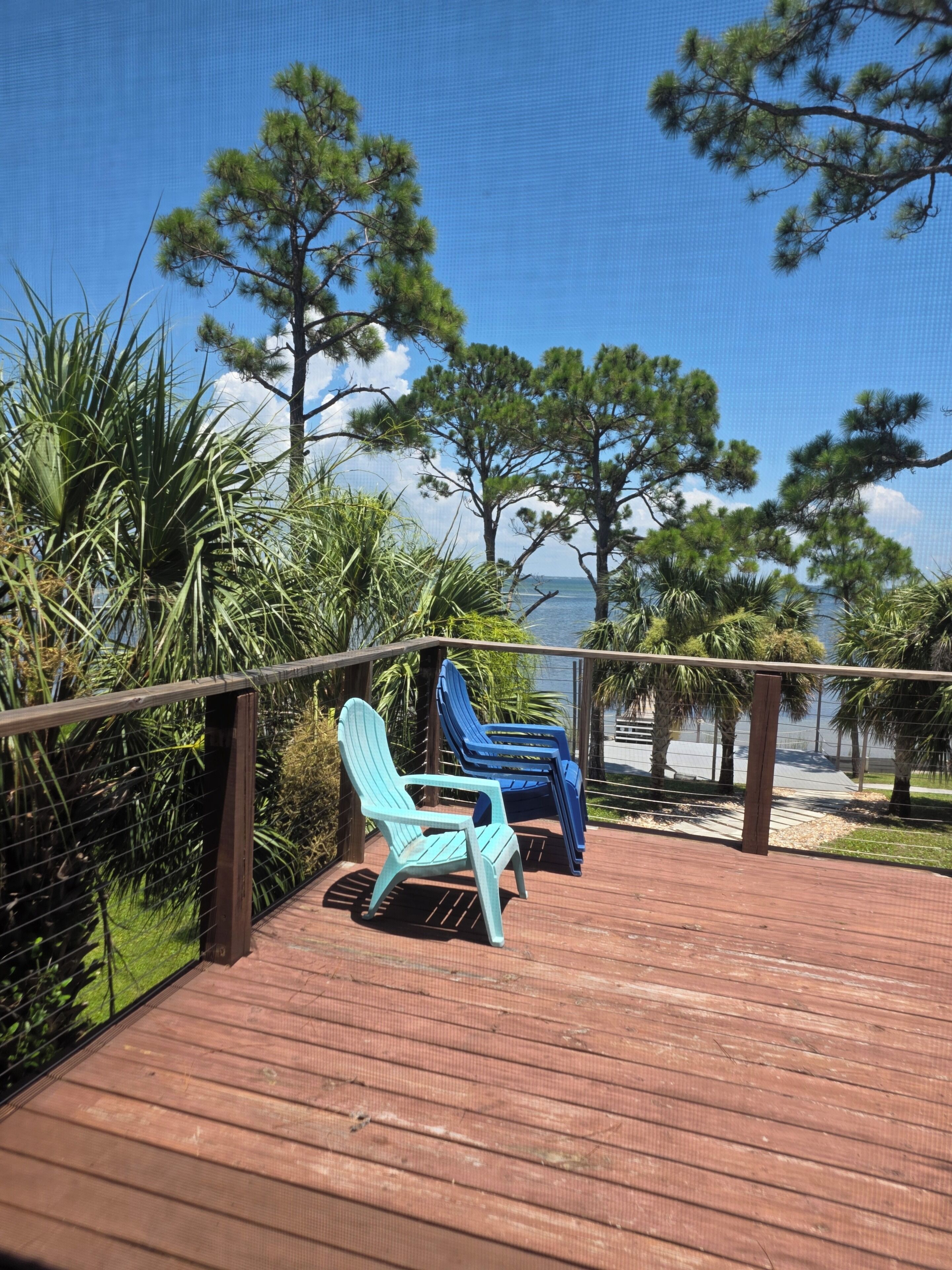 A wooden deck with two Adirondack chairs, surrounded by tropical vegetation and overlooking a body of water.