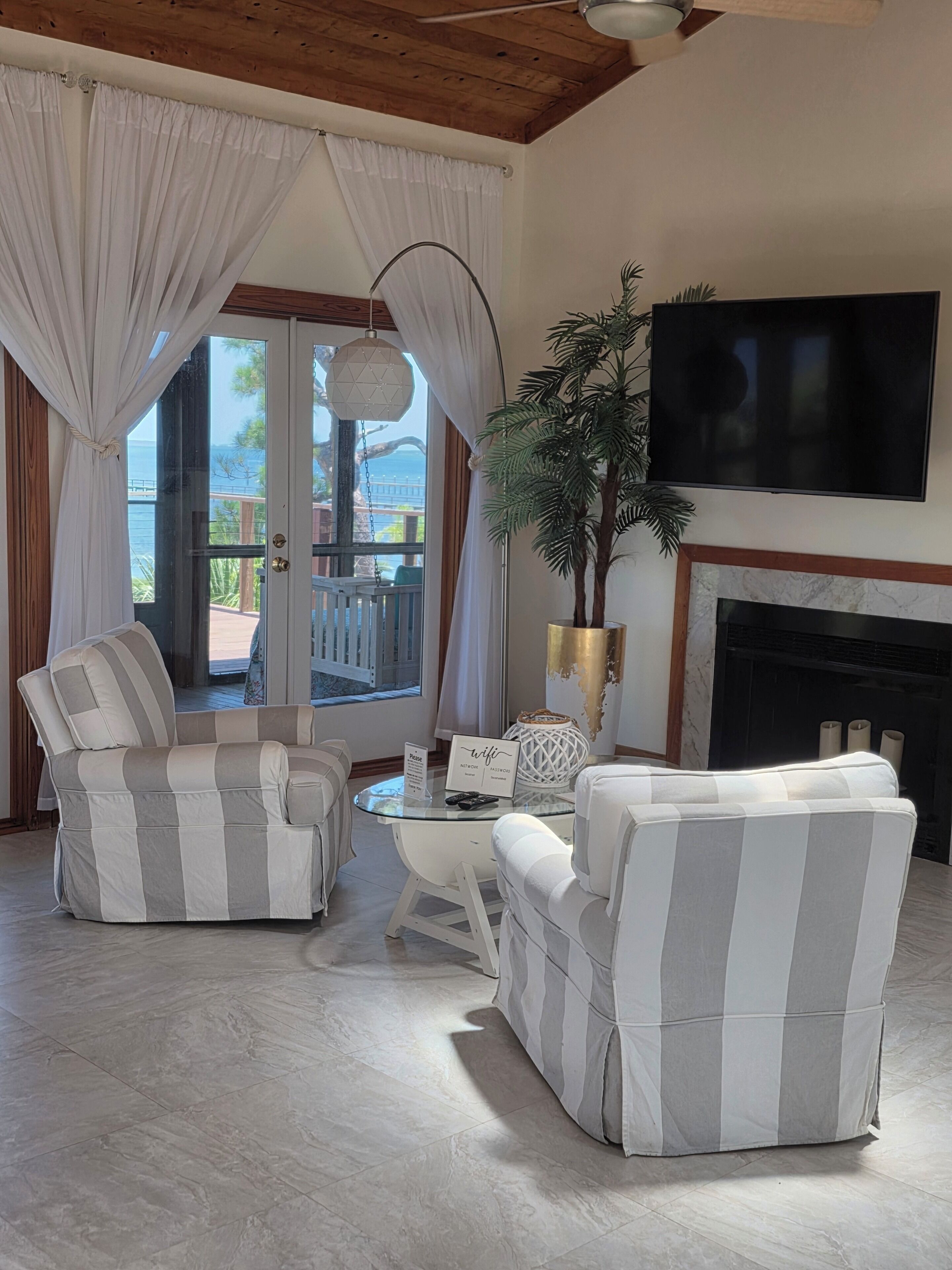 Un salon avec une cheminée, des canapés à rayures, une table basse et un téléviseur fixé au mur.