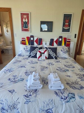 Ein Bett mit einem Bezug im maritimen Stil, Kissen mit der Aufschrift 'Gone' und ein Rettungsring mit dem Schild 'Bitte bleiben'.