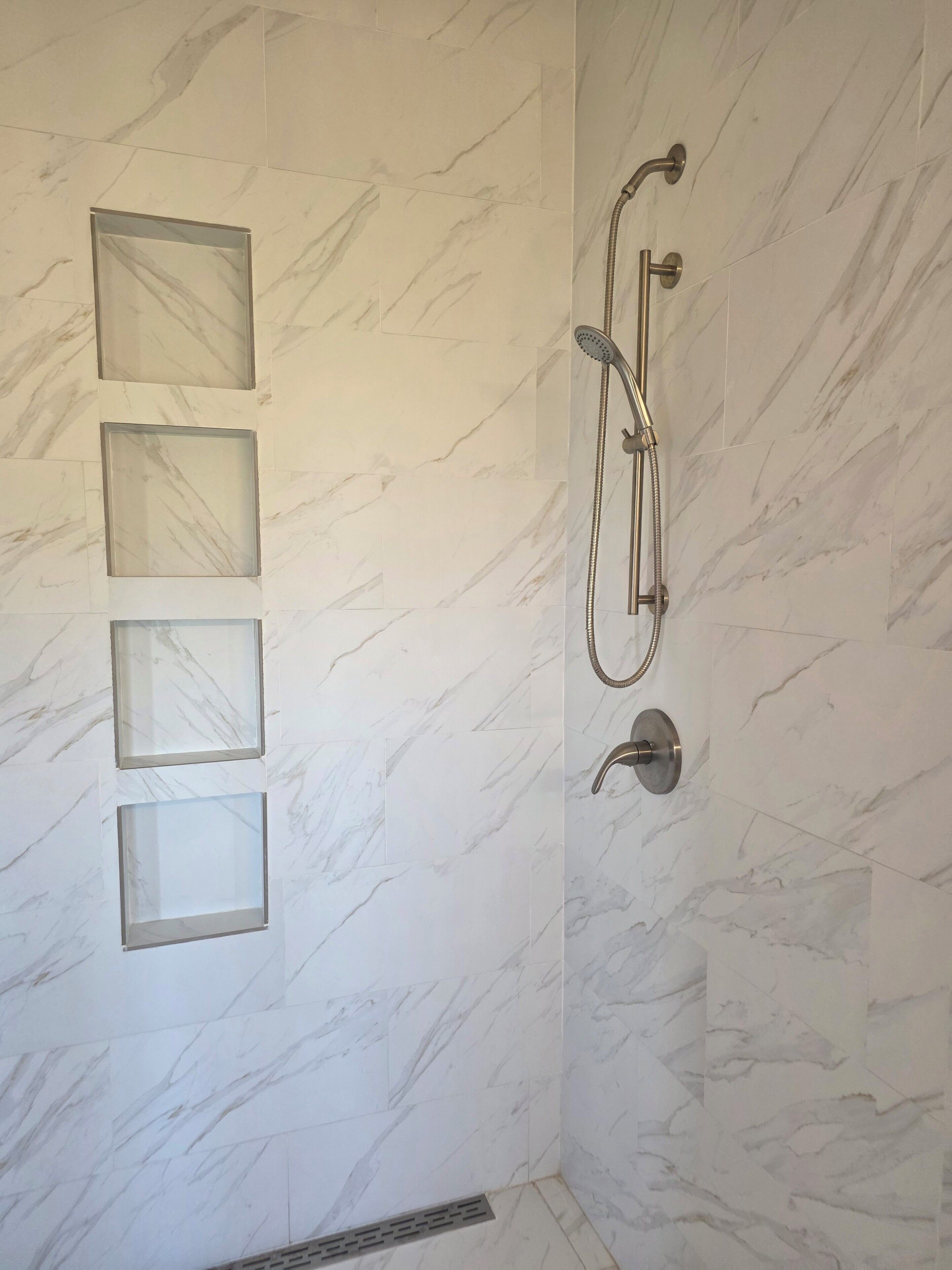 Een badkamer met een douche, marmeren wanden en een glazen wand.