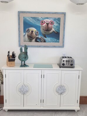 Ein weißer Schrank mit verzierten Muschelauschnitten, ein türkisfarbener Keramikfrosch, ein Messerblock und ein Toaster.