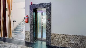 Un hall d’hôtel avec un sol en marbre, un extincteur fixé au mur, un escalier et une porte d’ascenseur en verre.