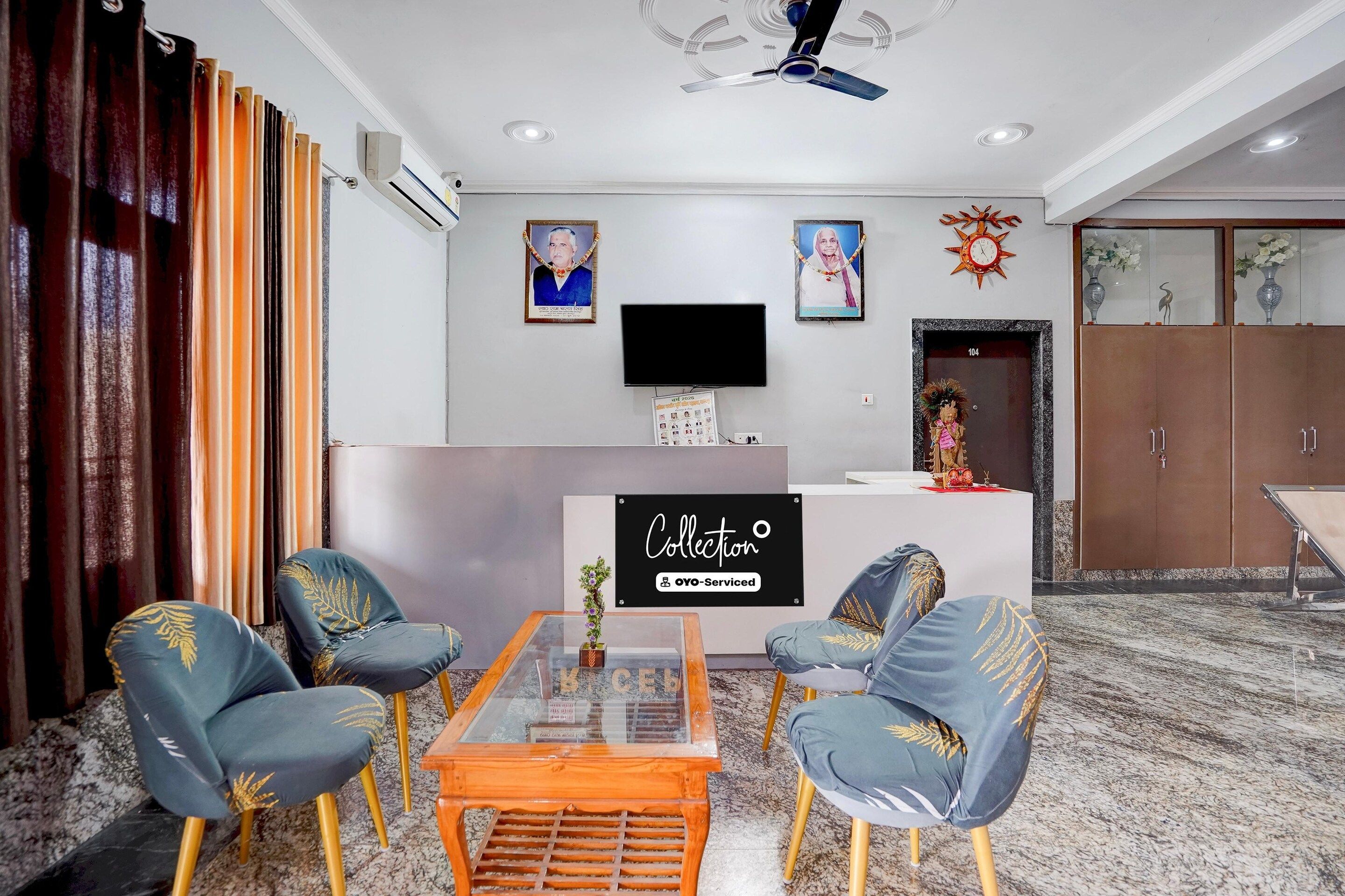 Un soggiorno moderno con un tavolino in vetro, due poltrone blu con decorazioni in foglia oro, un televisore a schermo piatto montato a parete e una scrivania reception con un cartello.