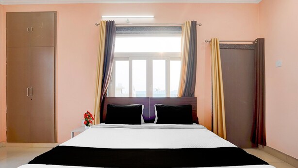 Une chambre d’hôtel avec un grand lit, deux tables de chevet, une armoire et une fenêtre avec des rideaux.