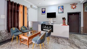 Un espace d’accueil d’hôtel comprenant un comptoir de réception, un téléviseur à écran plat, une photographie encadrée et une horloge décorative.