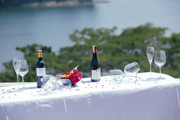 A table with wine bottles and glasses, a bouquet of flowers, and a scenic view in the background.