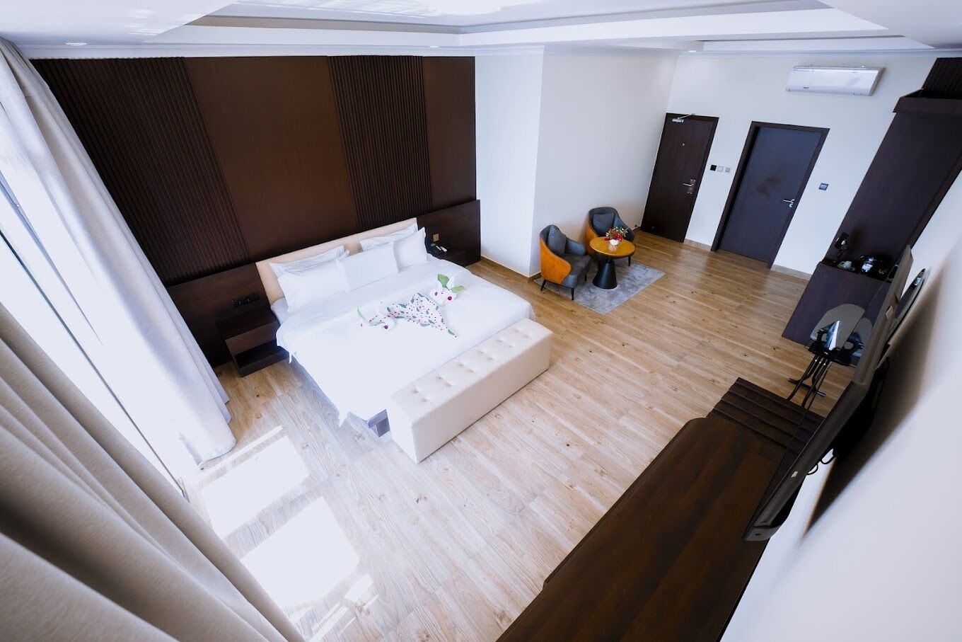 A modern hotel room with a large bed, a seating area with a small table, and a separate entrance door.