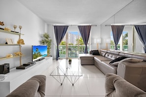 Een moderne woonkamer met een flatscreen televisie, een bank, een salontafel en een balkon met gordijnen.