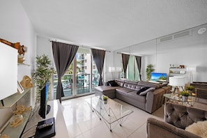 A modern living room with a sectional sofa, a glass coffee table, and a flat-screen TV. - Beautiful apartment in community with pool and beach in HOLLYWOOD BEACH MIAMI (Hollywood)
