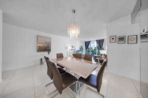 A modern dining area with a large table, chairs, a chandelier, and artwork on the walls. - Beautiful apartment in community with pool and beach in HOLLYWOOD BEACH MIAMI (Hollywood)