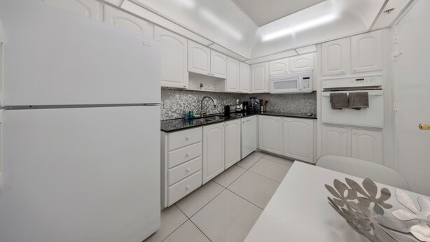 Cocina compacta con armarios blancos, encimera negra y microondas.