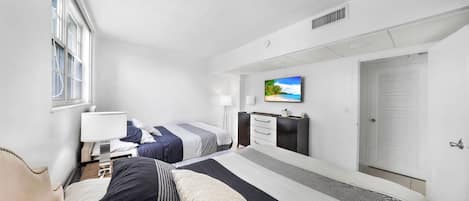 Habitación de hotel con dos camas, un televisor en la pared, un escritorio y una ventana.