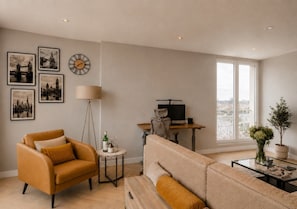 A living room with a sofa, armchair, and a desk with a computer. There are framed pictures on the wall and a lamp. - The Thames Horizon Luxury Skyline in Canary Wharf (London)
