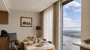 Un comedor con una mesa dispuesta para cuatro personas, una cafetera y vistas a un río a través de amplios ventanales.