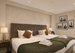 A hotel room with two beds, a large headboard, a green blanket, and a wall with framed pictures. - The Thames Horizon Luxury Skyline in Canary Wharf (London)