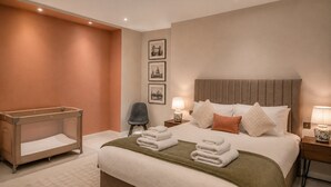 Una habitación de hotel con una cama grande, una mesita de noche, una silla y una cuna.