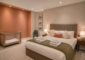Ein Hotelzimmer mit einem großen Bett, einem Nachttisch, einem Sessel und einem Babybett.