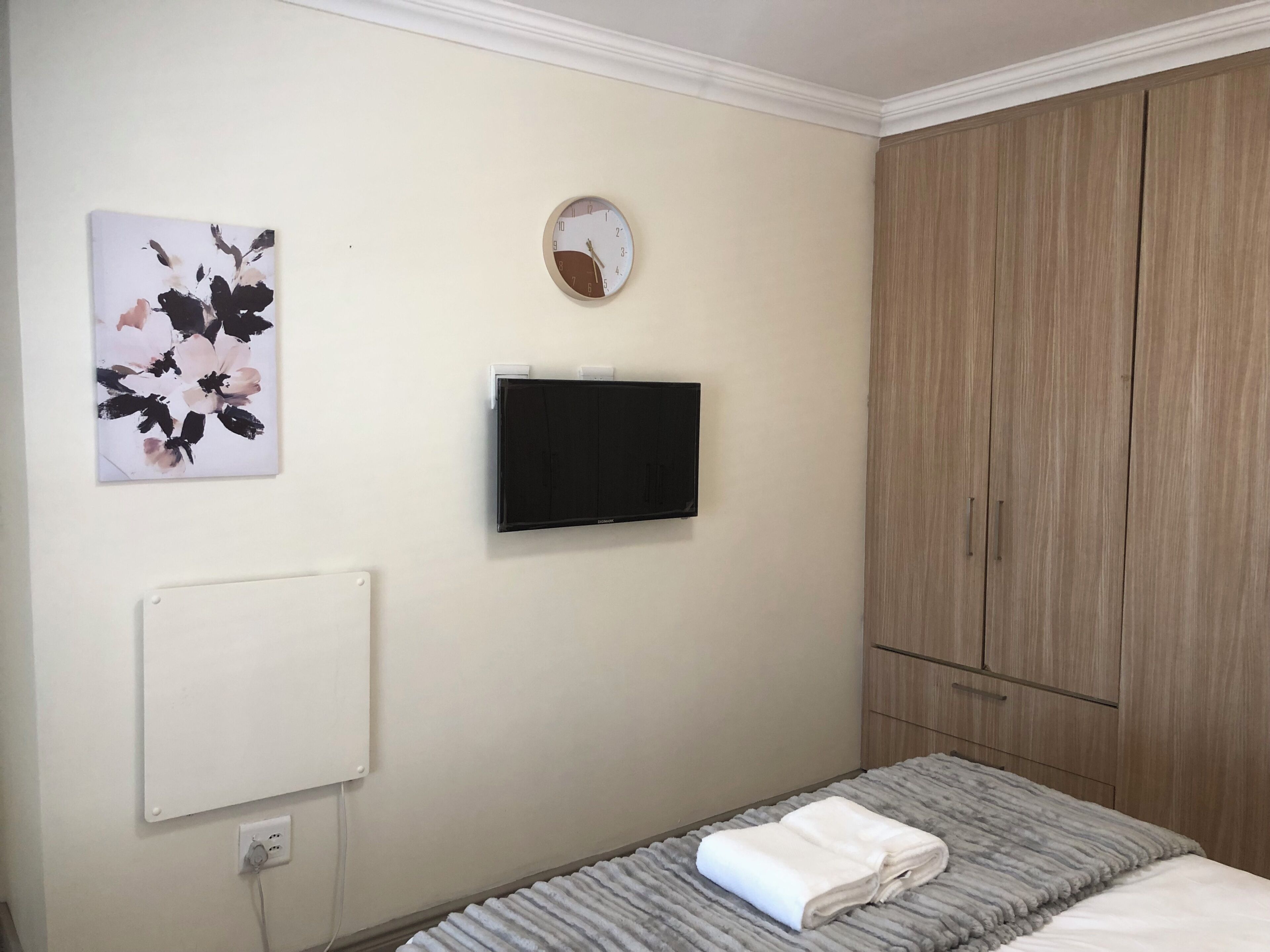 A bedroom with a bed, a wall-mounted TV, a radiator, a wardrobe, and a painting.