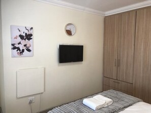 A bedroom with a bed, a wall-mounted TV, a radiator, a wardrobe, and a painting.
