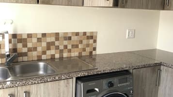 Una cucina con mobili in legno, un lavello in acciaio inossidabile, una parete rivestita di piastrelle e una lavatrice a carica frontale.