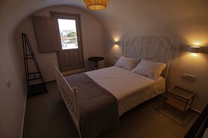 Ein Schlafzimmer mit einem Bett, einer Hockerleiter, einem kleinen Tisch und einer Wandleuchte.