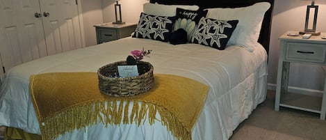 A neatly made bed with a decorative basket, two bedside tables with lamps, a door, and a wall with a painting.
