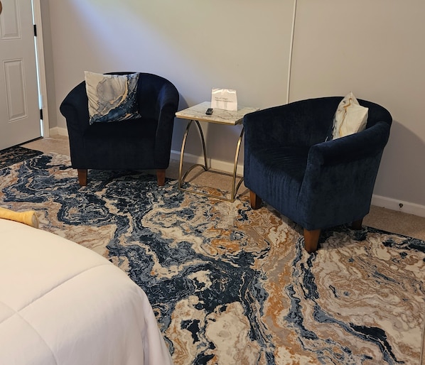 A hotel room with two armchairs, a small table, and a patterned rug.